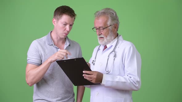 Senior Bearded Man Doctor Consulting Man Patient Against Green Background