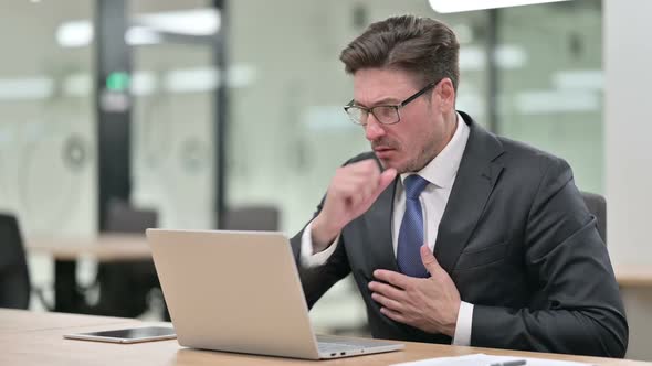 Sick Middle Aged Businessman with Laptop Coughing in Office