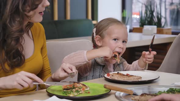 Portrait of Pretty Caucasian Daughter Eating Pizza in Restaurant Resting with Cheerful Mother