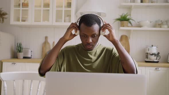 Young Black Man Freelancer Puts on Headphones and Works at Home on a Laptop