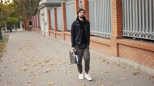 Man Walk Down the Street Holding a Guitar Case