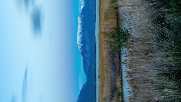 Vertical day-to-night time lapse of a river flowing into a lake with mountains in the background