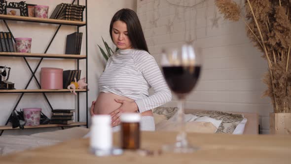 Glass of Wine and Pills on Table a Pregnant Woman is Sitting in the Background