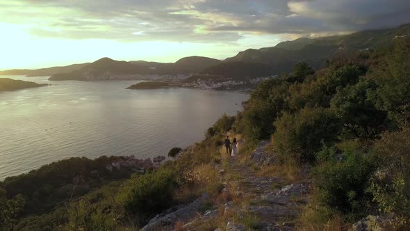 Aerial view of newlywed couple walks on a mountain in Montenegro at sunset