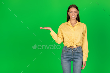  Smiling To Camera Advertising Great Product Standing Over Green Background. Studio Shot. Look At This Concept. Free Space