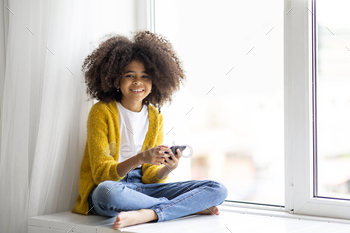 shy hair sitting on windowsill with smartphone, happy kid chatting with friends, using nice mobile application, home interior, copy space