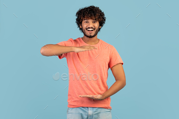 -shirt showing or holding something invisible in his hands and smiling at camera over blue studio background, copy space