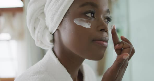 Portrait of african american attractive woman applying face cream in bathroom