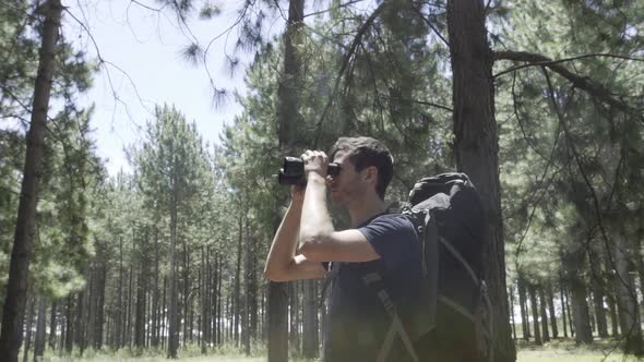 Hiker in forest looking through binoculars