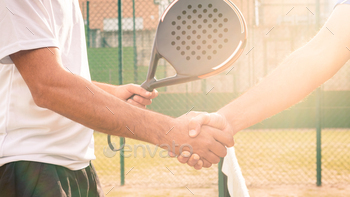 ch in a green paddel court outdoor. Tennis players shake hands with shining sun bright flash