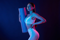 Young woman in sportive clothes is in the studio with neon lights. Holding mat - PhotoDune Item for Sale