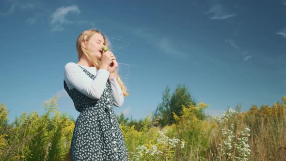 A Young Girl in a Beautiful Dress Sniffs Wildflowers