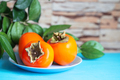 Persimmon on blue plate against background of green foliage and stone wall - PhotoDune Item for Sale