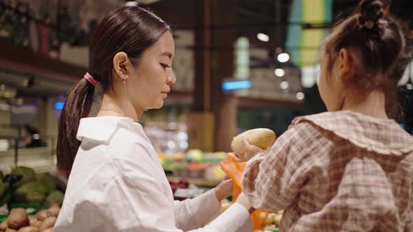 Preschooler Girl Helps Mother to Choose Potatoes in Market