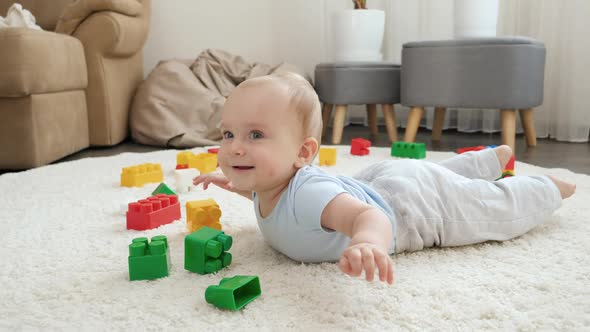 Happy Cheerfull Baby Boy Lying on Floor Next to Colroful Toys Bricks and Blocks at Playroom