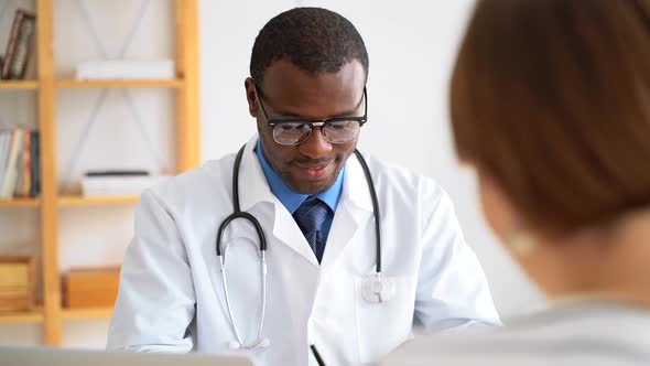 African American Male Doctor Communicates with Female Patient at Table in Modern Hospital Spbas