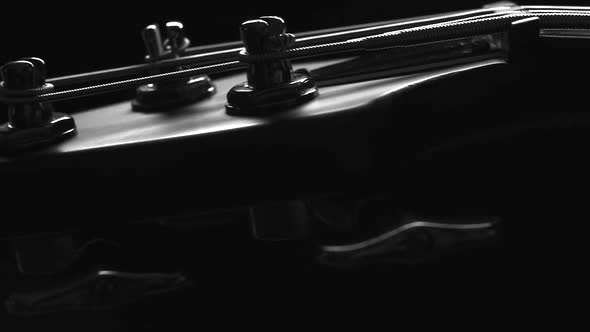 A headstock of a fretless electric bass guitar on the dark background, black and white, closeup