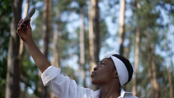 Confident Slim African American Young Woman Raising Hand with Smartphone at Background of Summer