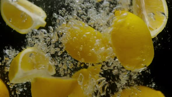 Closeup of Falling Sliced Lemons Into the Sparkling Water on Black Background Making a Cocktail of