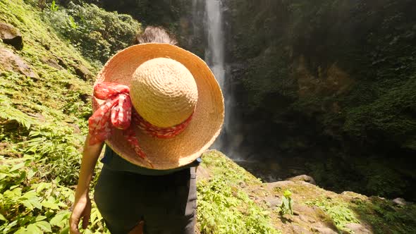 Young Traveler Girl Walking To Amazing Rainforest Jungle Waterfall and Raising Hands Up