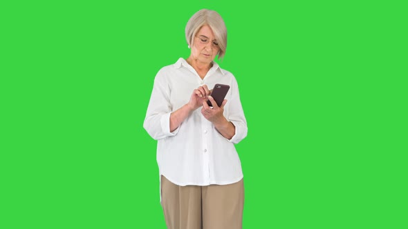 Stylish Mature Woman Typing Text Message on Mobile Phone on a Green Screen Chroma Key
