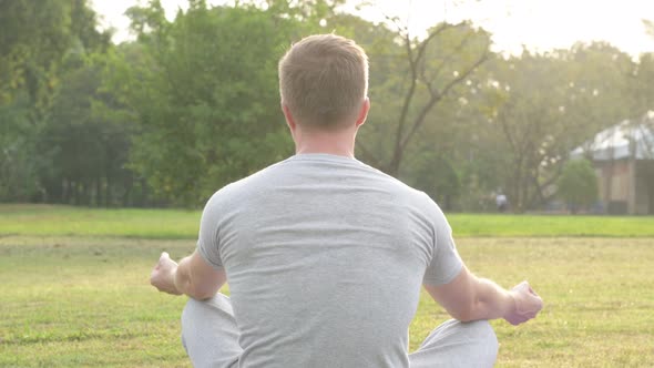 Rear View of Young Man Meditating at the Park