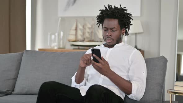 Excited African Man Having Success on Smartphone at Home 