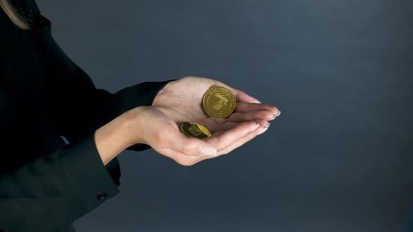 Female hands holding gold cryptocurrency coins, black blouse sleeves.