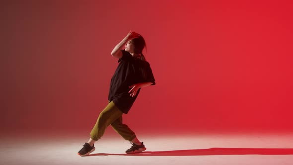 Brunette Woman Wearing Black Tshirt Dancing Contemporary on Red Neon Background in Studio