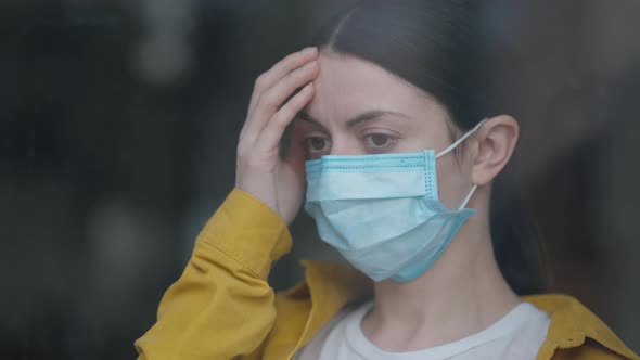 Headshot Portrait of Young Sad Caucasian Woman in Coronavirus Face Mask Standing Indoors Looking Out