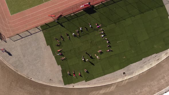 Kids doing situps by running track, top down rotating aerial