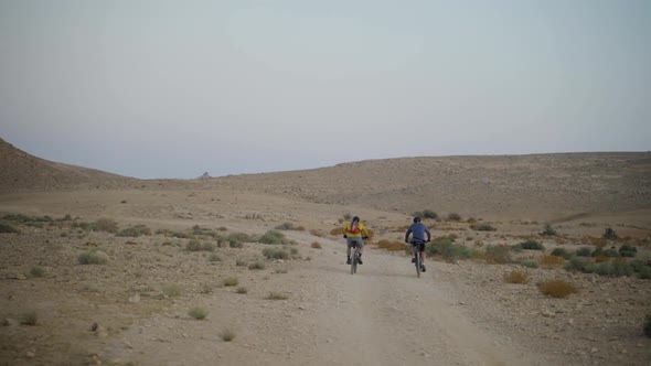 Two cyclers with mountain bikes ride off road in the desert landscape