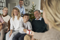 Caucasian boy giving Christmas present to his mom and family sitting around - PhotoDune Item for Sale