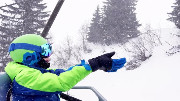 Boy Skier in Helmet Mask Down on the Ski Lift During Snowfall