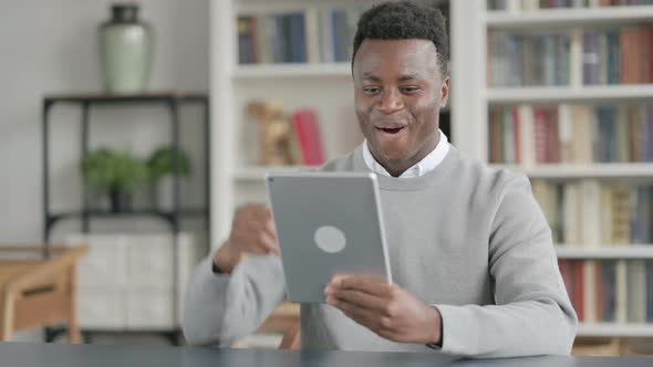 African Man Celebrating Success on Tablet in Library