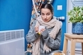 Teen female in sweater scarf warming near electric heating radiator, drinking hot drink - PhotoDune Item for Sale