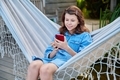Preteen girl sitting in hammock using smartphone for leisure study communication - PhotoDune Item for Sale