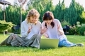 Teenage female student friends laughing sitting on grass with laptop - PhotoDune Item for Sale