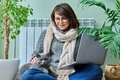 Middle-aged woman in warm clothes with cat using laptop at home - PhotoDune Item for Sale