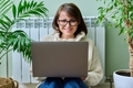 Woman in warm sweater using laptop sitting near heating radiator at home - PhotoDune Item for Sale