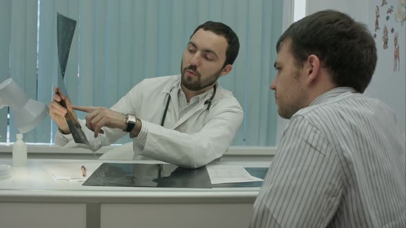 Male Bearded Doctor in Clinic Show X-rays To Male Client