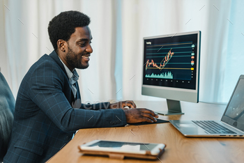 ing laptop and computer monitor with binary option charts while working at table