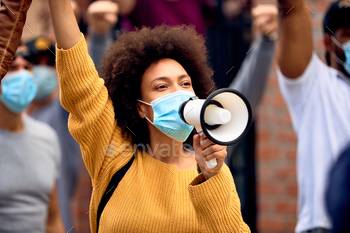 Black female activist wearing protective face mask while shouting through megaphone on a protest.