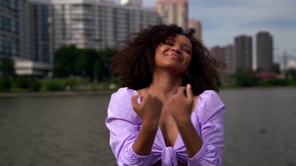 a Young African Woman Is Dressed in a Lilac Top with Ties and Puffy Sleeves. She Dances on the City