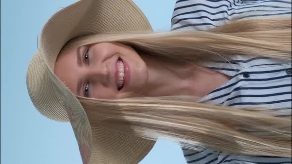 Beautiful Smiling Girl Putting a Hat on Her Head on Blue Background