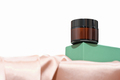 face cream in amber glass jar on green podium or pedestal on silk satin fabric.  - PhotoDune Item for Sale