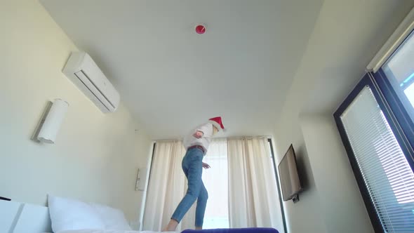 slender beautiful girl dancing in a Santa Claus hat on the bed.