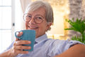 Portrait of beautiful senior woman sitting on sofa at home holding a coffee cup looking at camera sm - PhotoDune Item for Sale