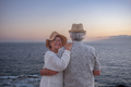 Cheerful senior couple hugging at the beach standing face the sea at sunset light. - PhotoDune Item for Sale