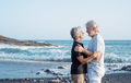 Lovely caucasian senior couple standing on the beach at sunset looking each other in the eyes - PhotoDune Item for Sale
